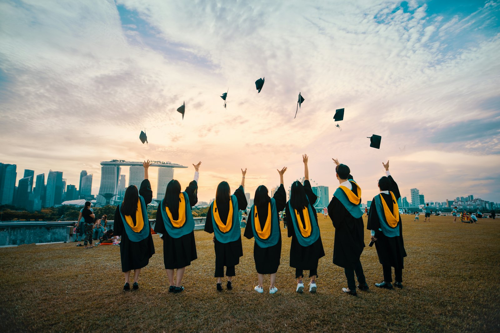 Graduates in gowns throwing their caps in the air at sunset.